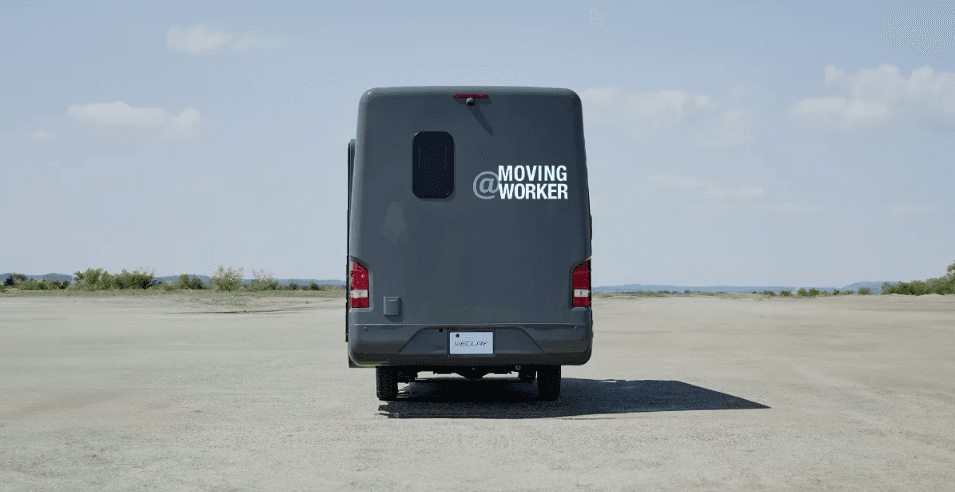 舗装のない広い野外に停車したVECLAY車両の後方。ナンバープレートと@ MOVING WORKERのグラフィックが見える